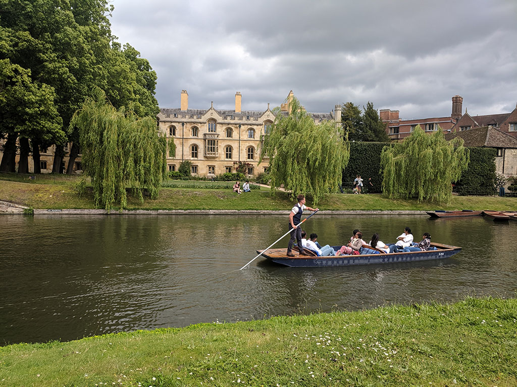 punting boat going down river cam with willow trees and historical tan buildng in background