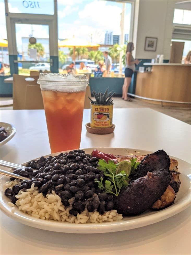 plate with plantains chicken rice black beans and ice tea and lime juice