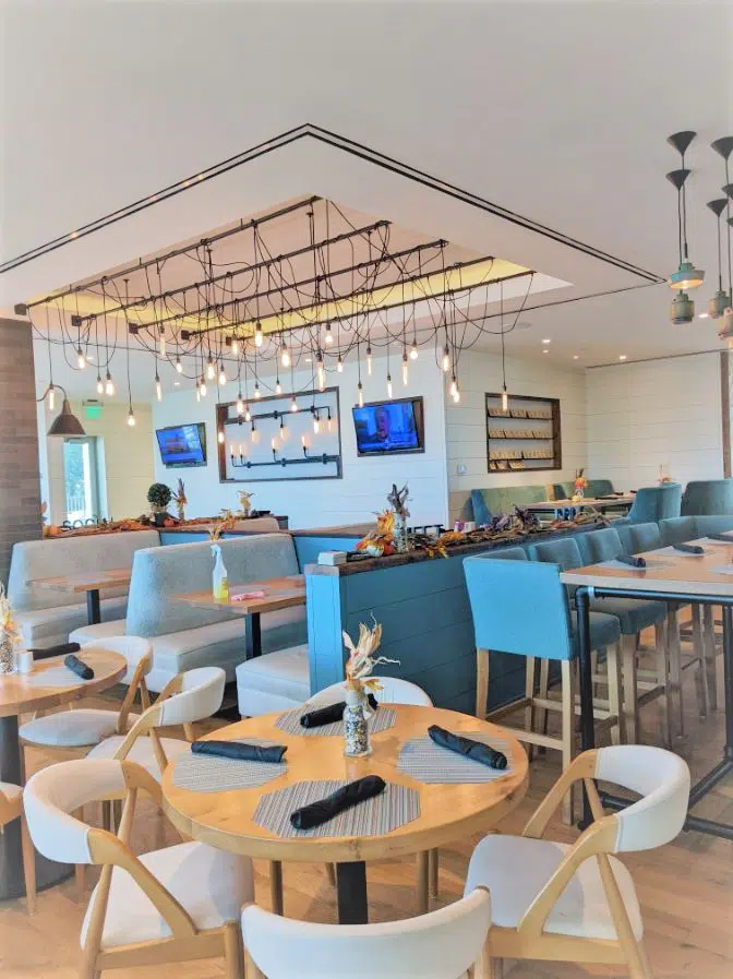 restaurant dining room with white and wood chairs blue benches and black string lights