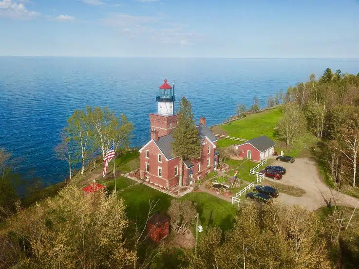 drone angle of red brick lighthouse on the coast of a lake with dirt parking lot