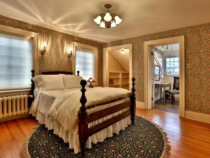 dark floral wallpaper and victorian style wooden bedfram with white bedding and floral circle run connected to a small sitting room