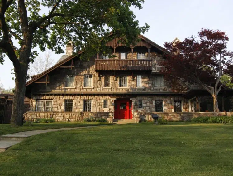 a frame brick house with third floor patio and a bright red door with trees