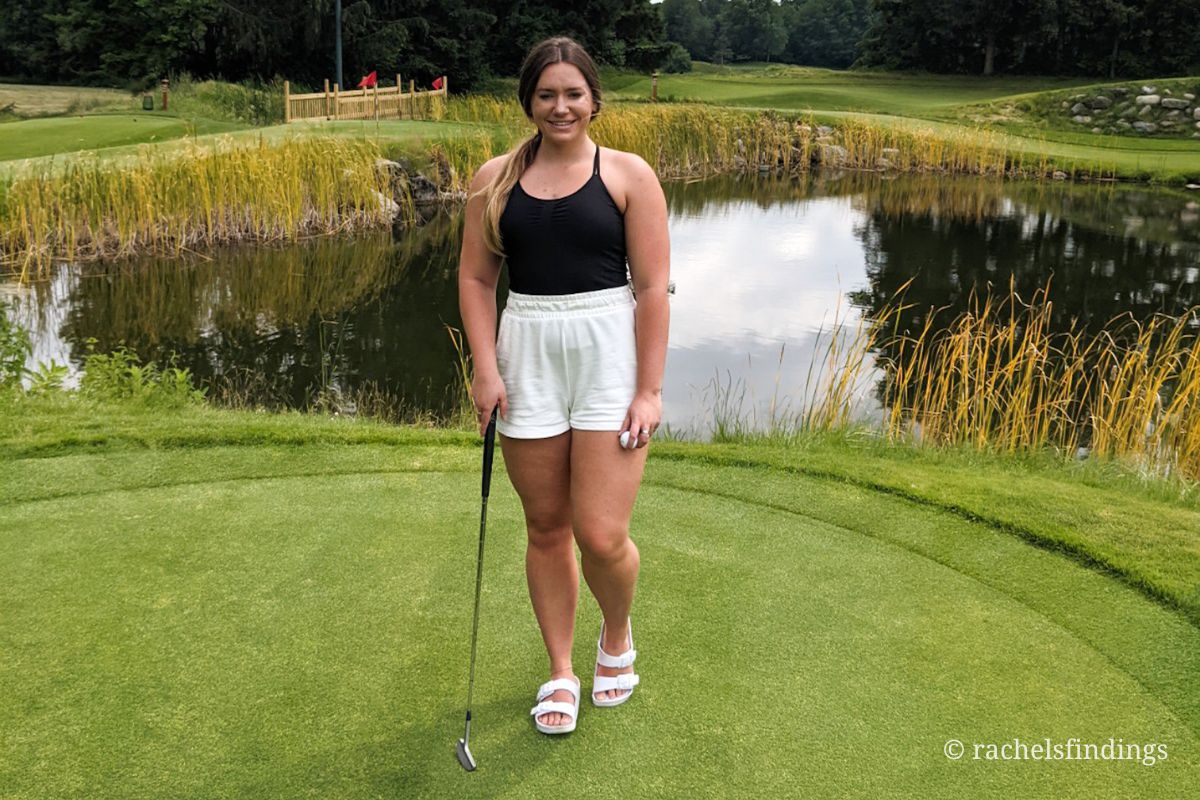 girl with golf putter on the green in front of pond