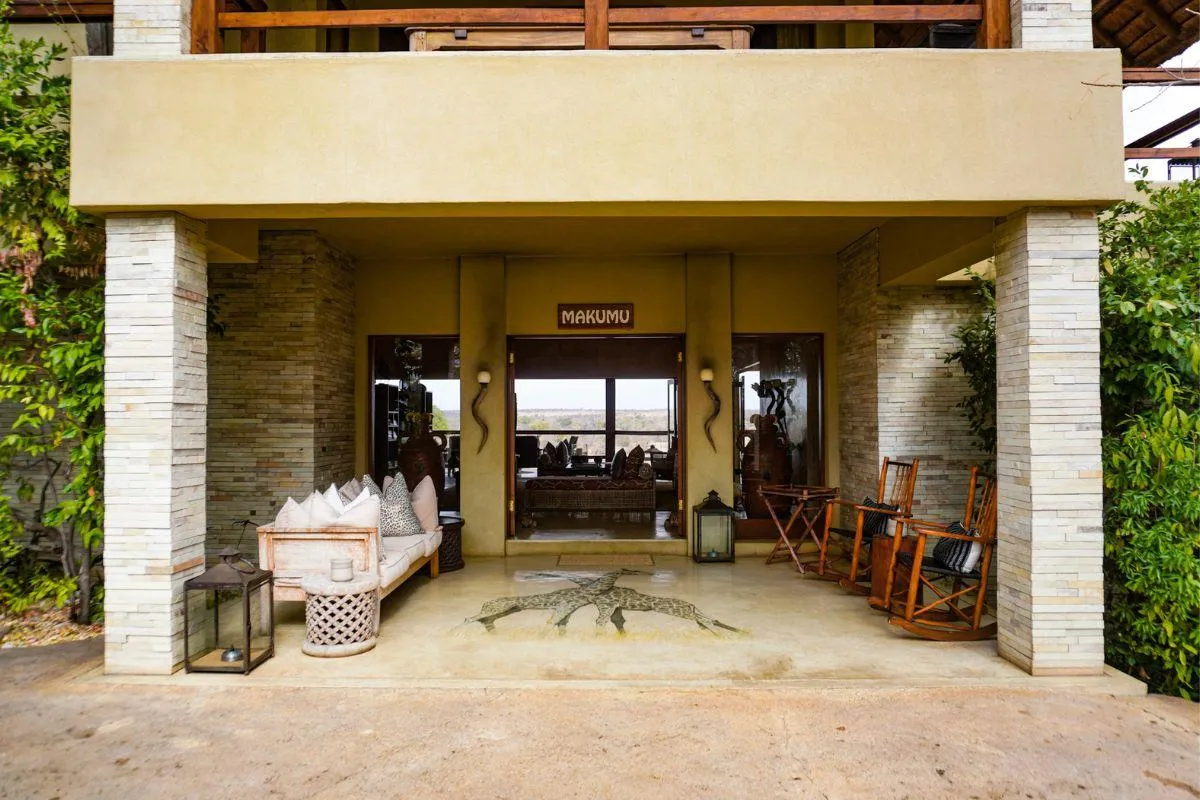 Welcoming entrance of the Makumu Lodge featuring natural stone columns, rustic seating, and decorative elements that reflect a charming safari atmosphere.